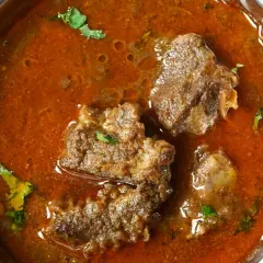 Un invitante buglione di agnello in una ciotola metallica, con pezzi di carne tenera immersi in un ricco sugo speziato e guarnito con erbe fresche.