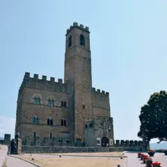 Un antico borgo alla collina domina il paesaggio, con un imponente torrione che svetta verso il cielo azzurro.