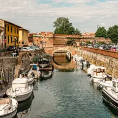 Canali di Livorno, un'ottima idea per cosa vedere in 2 giorni: barche ormeggiate lungo i muri di mattoni, un ponte ad arco e palazzi storici.
