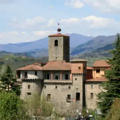La Rocca Ariostesca domina il borgo con la sua torre imponente, circondata da colline verdi e un cielo azzurro con nuvole bianche.