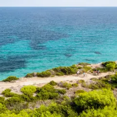 Ciclisti esplorano la costa dell'isola di Pianosa, con acque cristalline e vegetazione mediterranea.