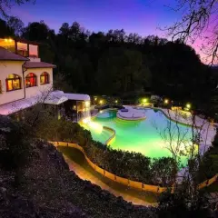 Piscina illuminata e un edificio a San Carlo Terme al tramonto, con cielo viola e rosa.