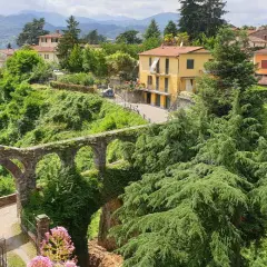 Un antico acquedotto in pietra, ricoperto di vegetazione, domina il paesaggio collinare dove si trova Barga. Case gialle e arancioni si stagliano tra il verde lussureggiante.