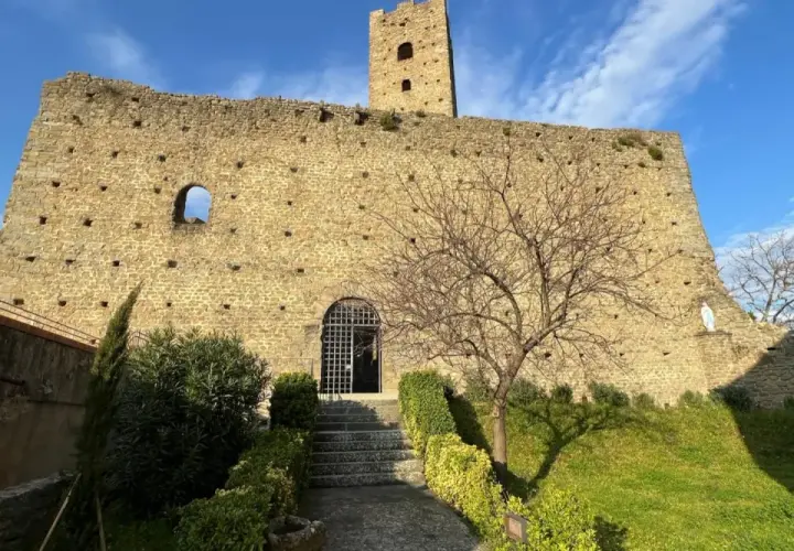 Rovine del castello di Larciano Pistoia, con torre, mura in pietra e un piccolo giardino curato.