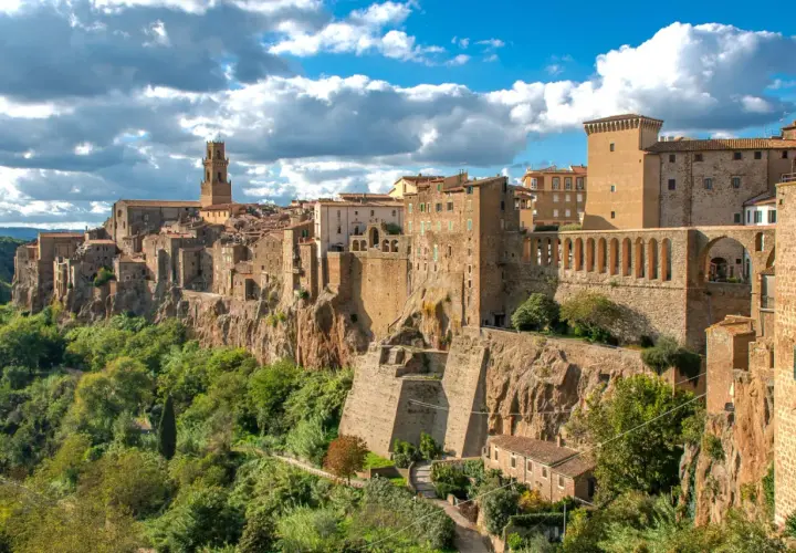 Un borgo arroccato su una rupe, con case in pietra e un campanile svettante, sembra una piccola Gerusalemme sotto un cielo azzurro e nuvoloso.