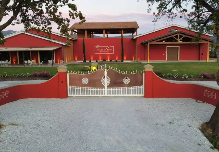 L'ingresso della Tenuta di Vaira a Bolgheri, con cancelli in rame e bianco, edifici rossi e un prato curato.
