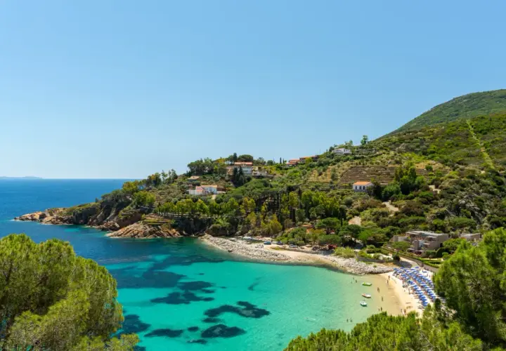 Incantevole baia con acque cristalline, spiagge dorate e case arroccate sulle colline verdi, un sogno di città toscane sul mare.