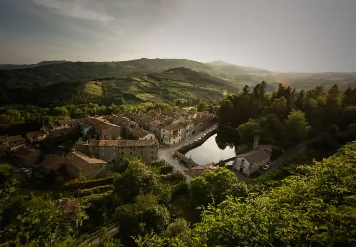 Peschiera Santa Fiora, un borgo toscano incastonato tra colline verdi, con case in pietra e un laghetto che riflette il cielo.