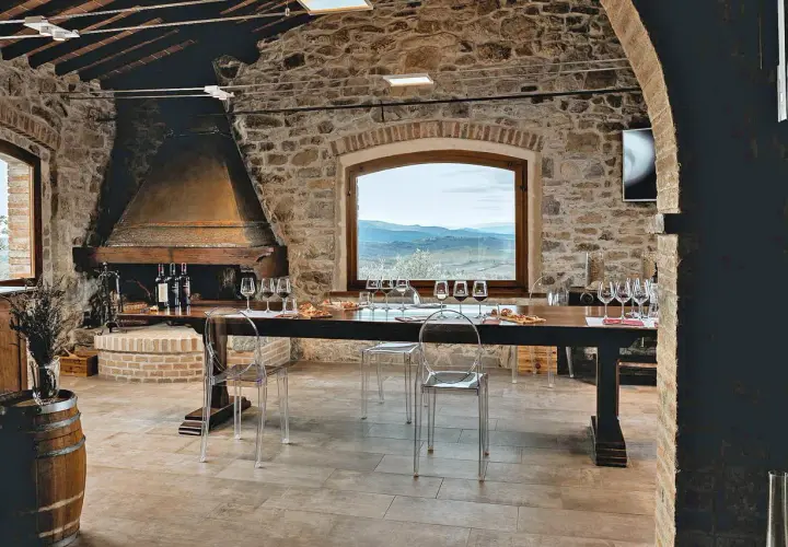 Sala degustazione in pietra con camino, tavola apparecchiata per assaggio vini, vista panoramica sulle colline del Chianti.