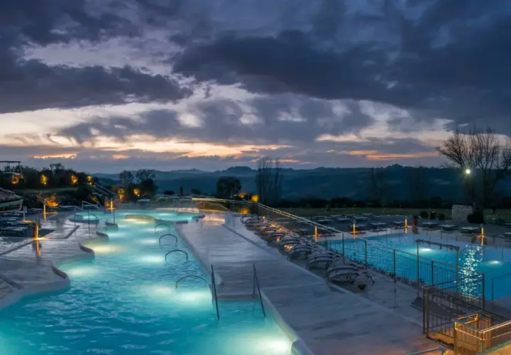 Piscine termali illuminate a Rapolano Terme al tramonto, con un cielo drammatico e colline toscane sullo sfondo.