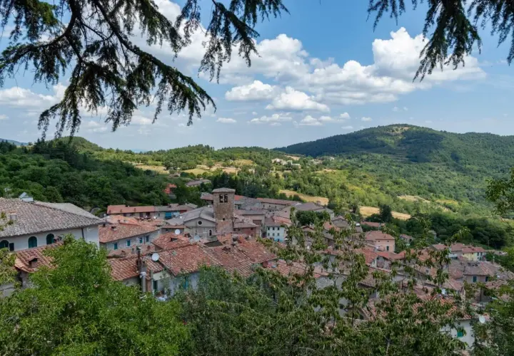 Panoramica di Montieri, Grosseto, con tetti in cotto e colline verdi sotto un cielo azzurro con nuvole bianche.