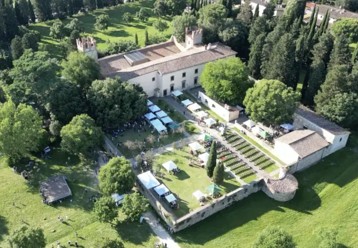 Mercato all'aperto nel parco dell'Acciaiolo, con bancarelle, persone e un edificio storico circondato da alberi.