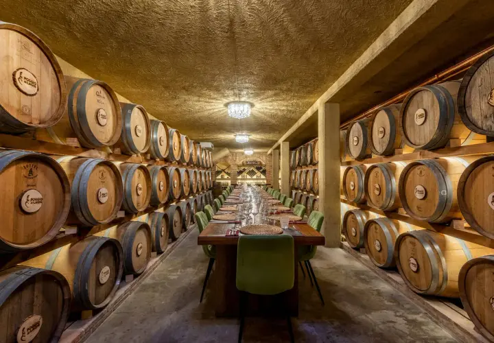 Un'elegante sala per una visita in cantina con degustazione, con botti di legno disposte su entrambi i lati e un lungo tavolo apparecchiato.