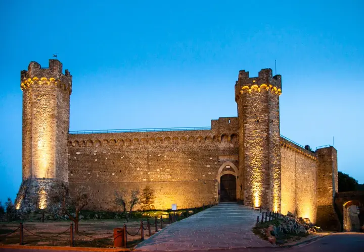 Fortezza illuminata al crepuscolo, un invito a visitare Montalcino e scoprire la sua storia.