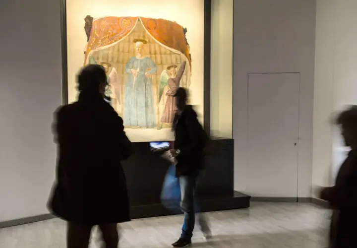 La Madonna del Parto di Piero della Francesca, con visitatori che la ammirano in un museo.