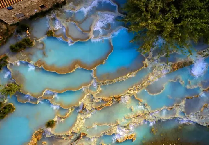 Cascate naturali di acqua turchese in un thermal spa Tuscany, con una persona che si rilassa tra le rocce calcaree.