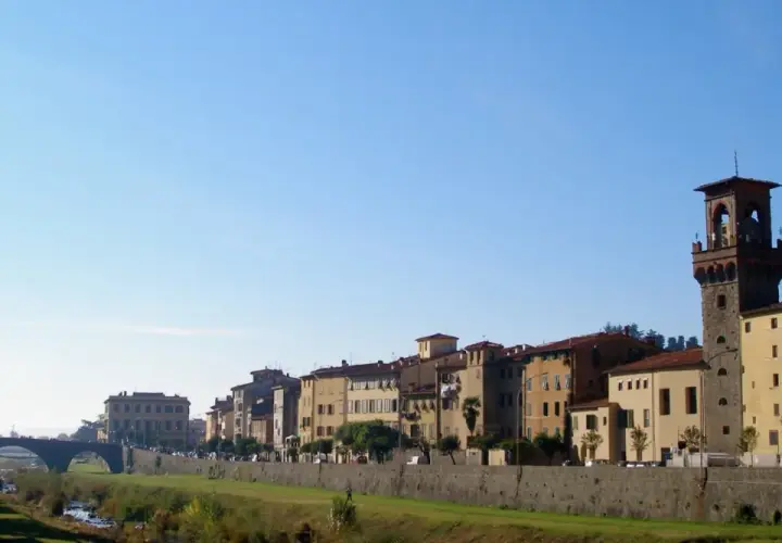 Edifici storici e una torre medievale si affacciano sul fiume nel pescia centro storico, sotto un cielo azzurro.