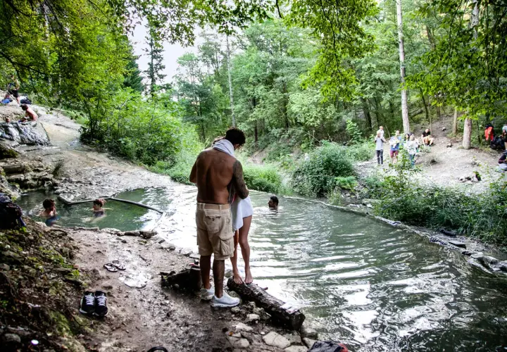 Persone si godono le acque termali ai Bagni San Filippo, un'oasi naturale in un bosco rigoglioso. Nonostante il nome, l'immagine evoca un'atmosfera estiva, non invernale.