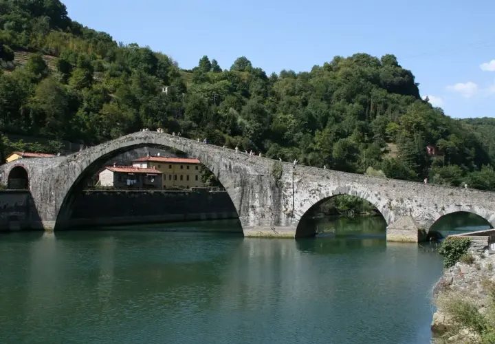 Il Ponte del Diavolo, con i suoi archi in pietra, attraversa un fiume verdeggiante, circondato da colline boscose.