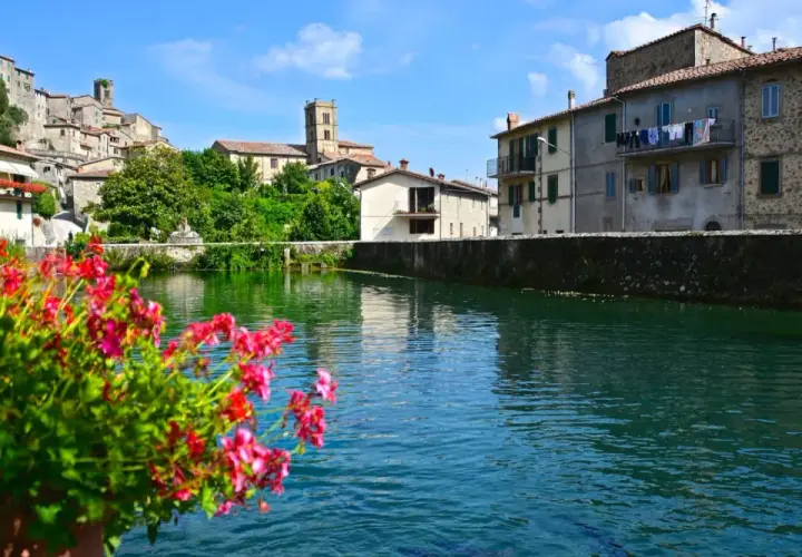 Fiori rossi in primo piano, con il borgo di Santa Fiora, Grosseto, che si specchia nell'acqua limpida.