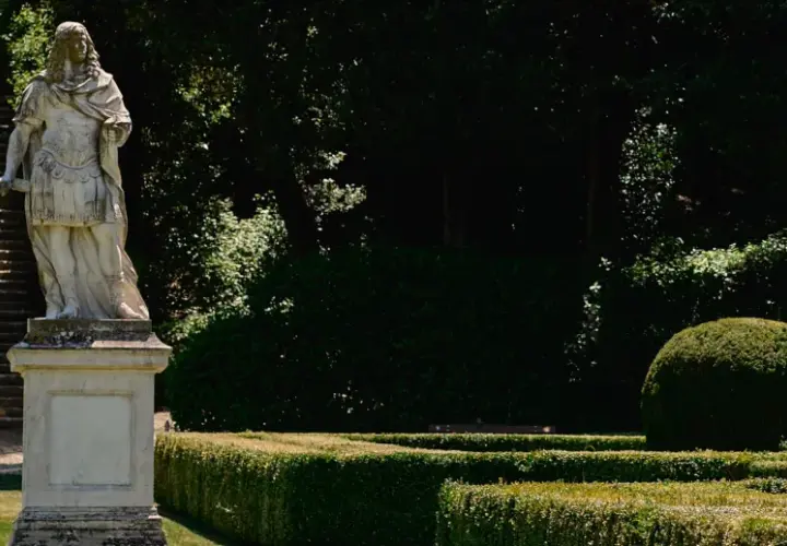 Statua romana domina una scalinata nei **Horti Leonini**. Giardini curati e alberi ombrosi creano un'atmosfera serena.