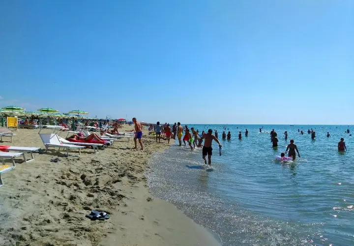 Una giornata di sole a Marina di Tirrenia, con bagnanti che si godono il mare e la spiaggia affollata di ombrelloni e lettini.