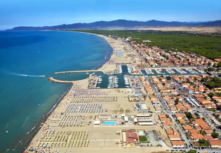 Vista aerea di Marina di Grosseto con spiaggia affollata, porto turistico pieno di barche e case con tetti rossi.