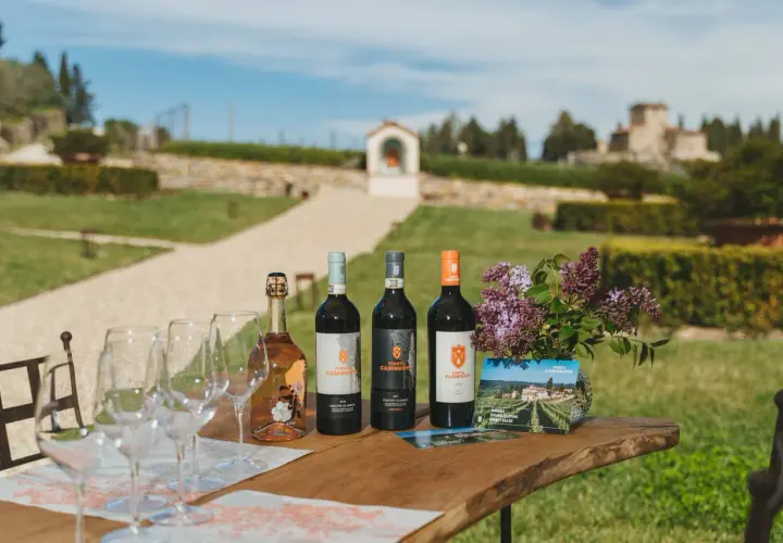 Vino e bicchieri sul tavolo di legno, con la campagna toscana e la Tenuta Casenuove sullo sfondo.