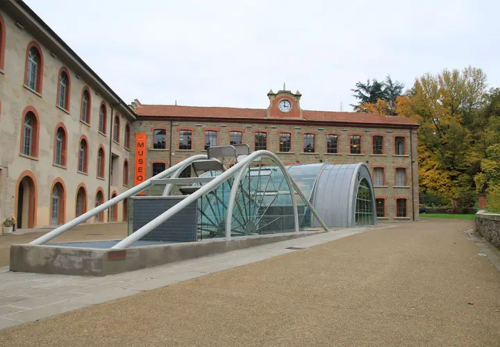 Edificio moderno con struttura in vetro e metallo accanto a un edificio storico, con insegna "MUSEO" a **stia Arezzo**.