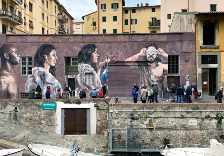 Un imponente murales livornese raffigura tre volti, uno bendato, con persone che osservano l'opera d'arte.