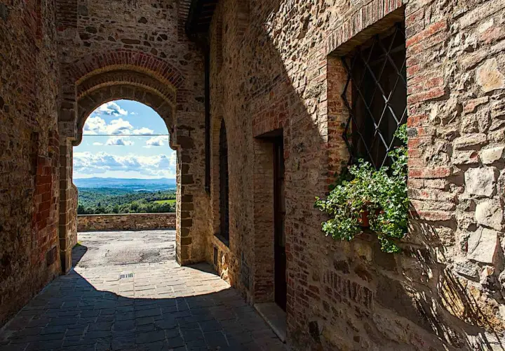 Un vicolo in pietra a San Gusmè, con un arco che rivela un paesaggio collinare toscano.
