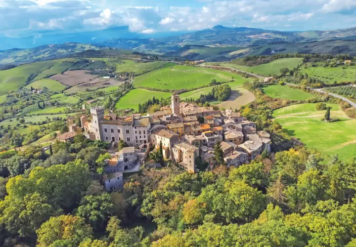 Un borgo toscano arroccato su una collina, circondato da dolci colline verdi e campi coltivati. Un esempio dei borghi toscani più belli.