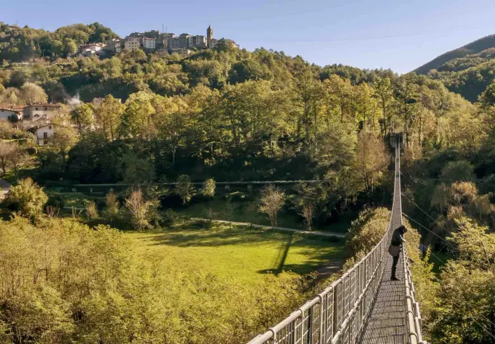 Una persona osserva il panorama dal ponte sospeso delle Ferriere, con un borgo arroccato sulla collina sullo sfondo.