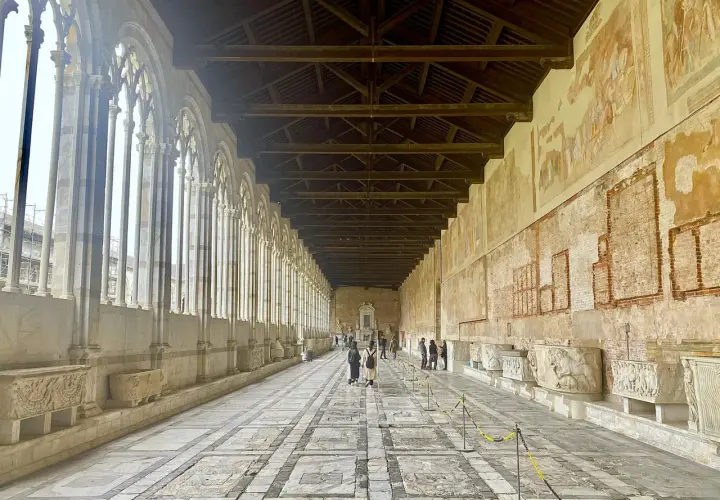 Corridoio del Camposanto Monumentale di Pisa con arcate gotiche, affreschi antichi e sarcofagi romani.
