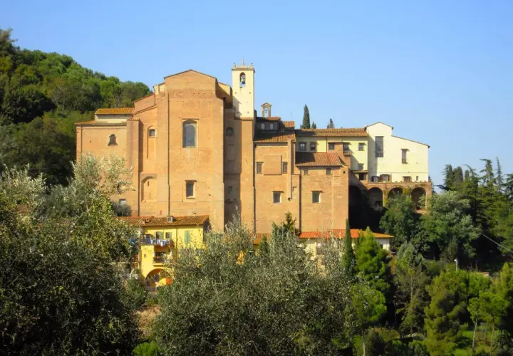 Il convento San Francesco a San Miniato, con la sua imponente struttura in mattoni rossi, si staglia tra il verde degli alberi e il cielo azzurro.