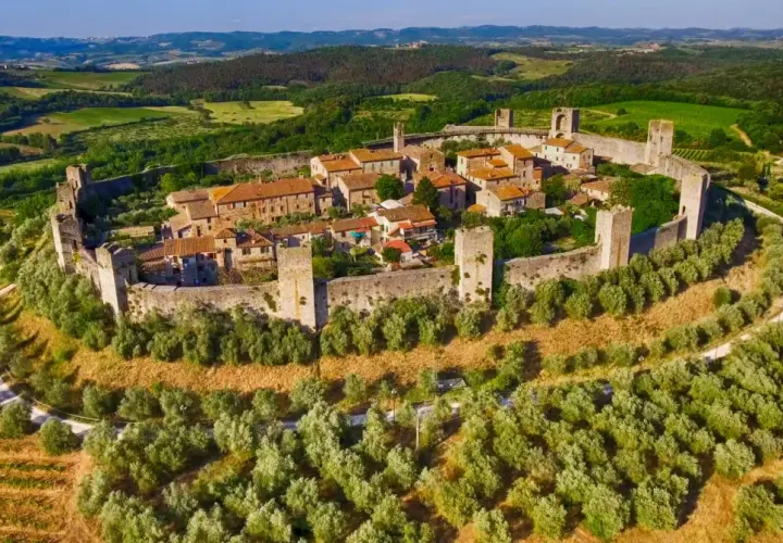 Il centro storico di Monteriggioni, un borgo medievale fortificato, si erge su una collina circondato da mura e torri, immerso nel verde della campagna toscana.