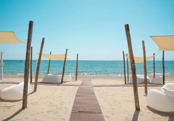 Un percorso in legno conduce al **follonica mare**, dove lettini bianchi e tende color crema invitano al relax sotto il sole.