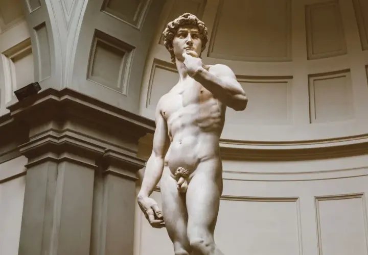 Michelangelo's David statue, a marble sculpture of a nude male figure, stands in a grand hall.