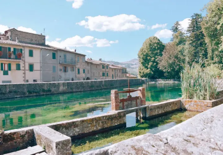 Un canale d'acqua cristallina attraversa un borgo con case antiche, ricordando i pittoreschi **paesi vicini al Monte Amiata**.