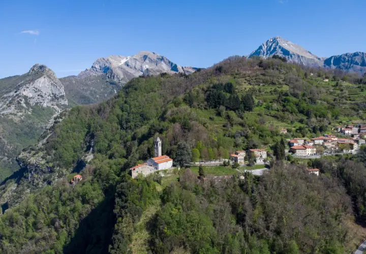 Sant'Anna di Stazzema: un borgo tra monti verdi e cielo azzurro. La chiesa domina il paesaggio, un luogo da scoprire.
