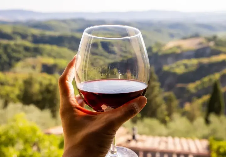 Un bicchiere di vino rosso, forse il miglior Morellino di Scansano, con un panorama collinare toscano sullo sfondo.