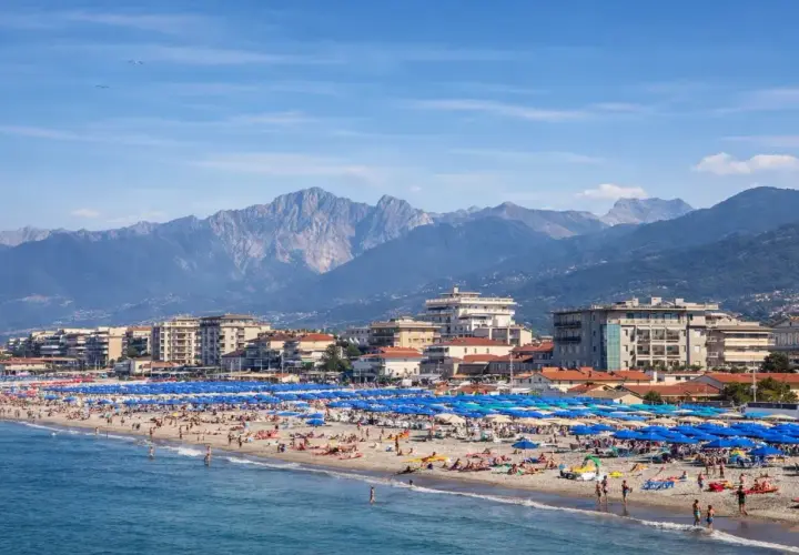 Una vivace spiaggia libera al Lido di Camaiore, con montagne imponenti sullo sfondo e un mare azzurro.
