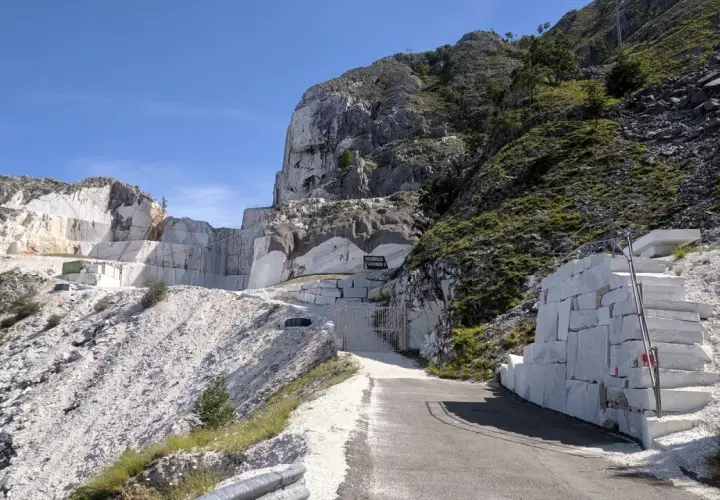 Un imponente passo del vestito di marmo bianco si erge su un fianco della montagna, con blocchi grezzi e una scala scavata nella roccia.