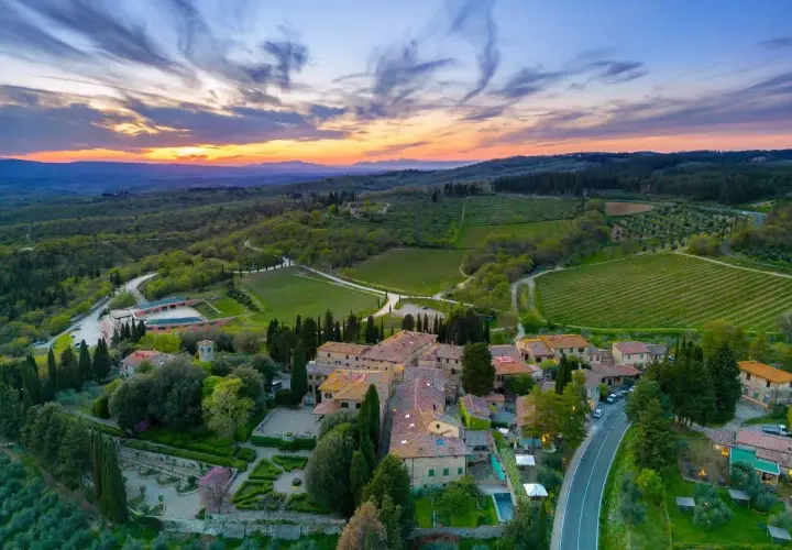 Tramonto mozzafiato sulla **chianti region**, con vigneti rigogliosi e un borgo toscano che si illumina sotto il cielo colorato.