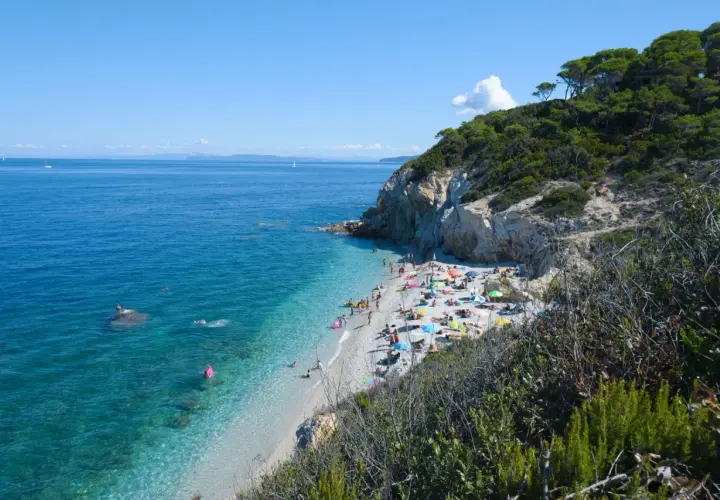 Spiaggia affollata vicino a Campiglia Marittima, con gente che prende il sole e nuota nelle acque cristalline.