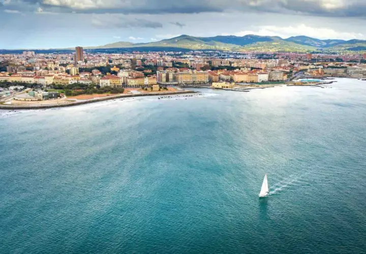 Un veliero solca il mare di Livorno, con la città e le colline sullo sfondo.