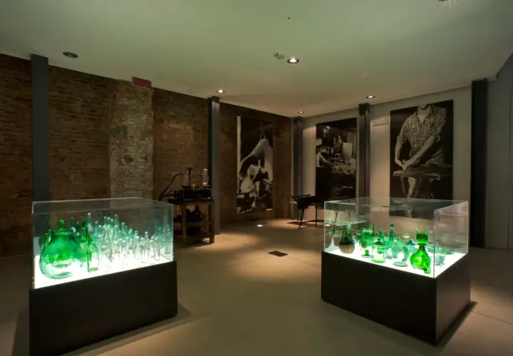 Vetrina con bottiglie verdi illuminate, un'esposizione che racconta cosa vedere a Empoli, tra storia e arte del vetro.