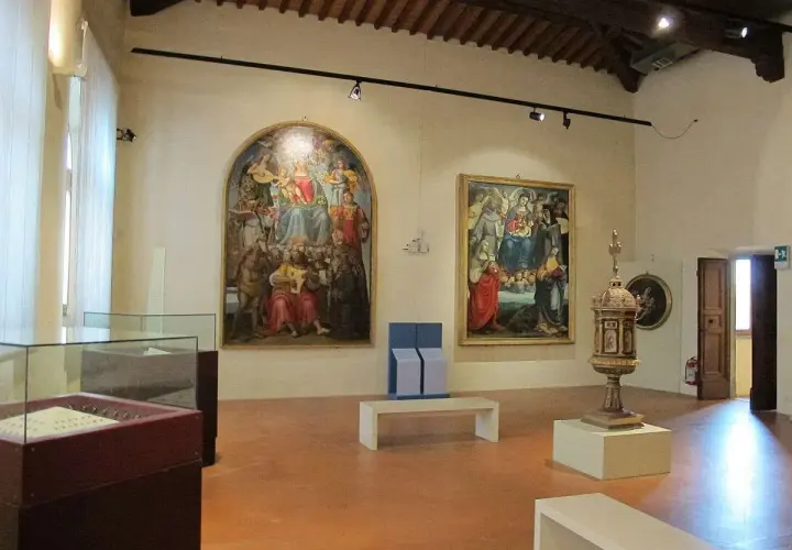 Interno di una sala dei musei di Arezzo con dipinti rinascimentali, un'urna e teche espositive.