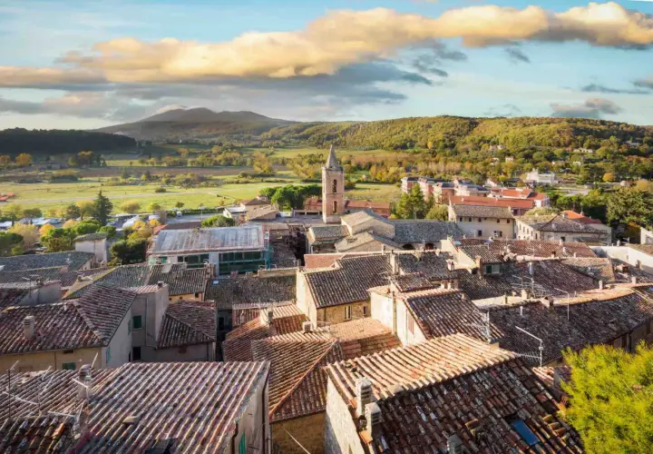 Panoramica di Sarteano cosa vedere: tetti in cotto, campanile e colline verdi sotto un cielo nuvoloso.