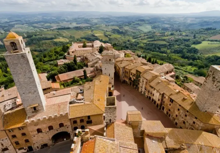 Panoramica aerea di San Gimignano, con le sue torri medievali che svettano tra i tetti di tegole rosse. Un paesaggio incantevole, tipico dei borghi vicino San Gimignano, immerso nel verde delle colline toscane.